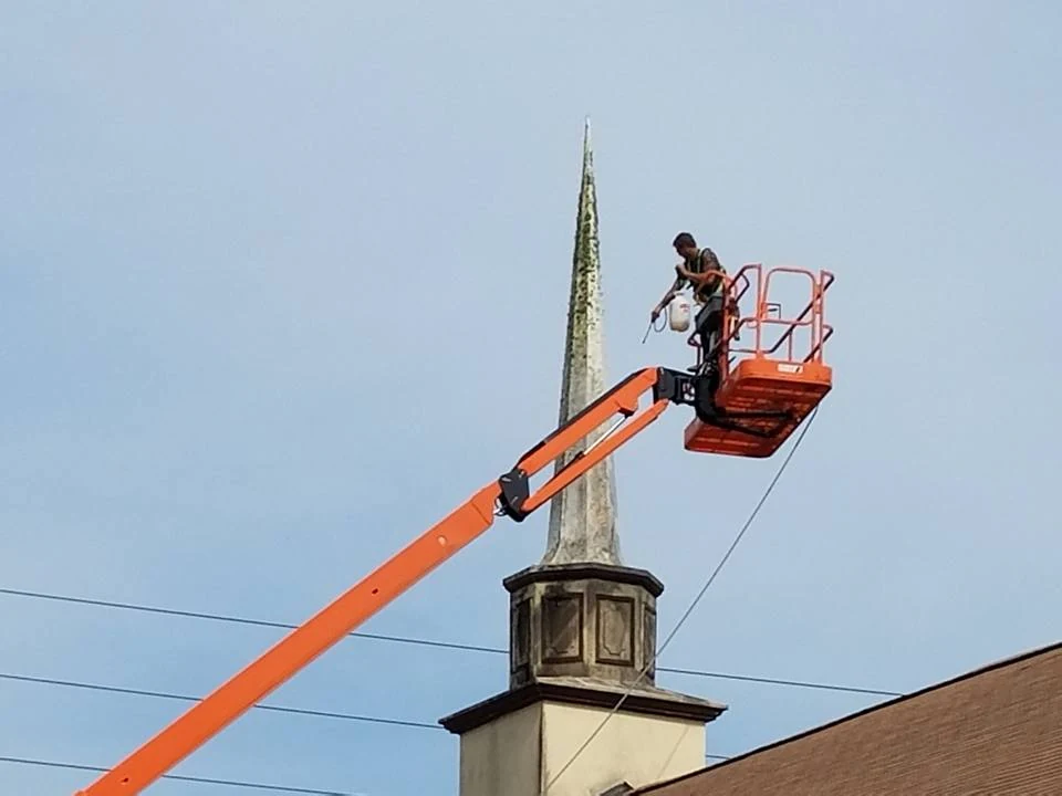 Worker cleaning a church steeple from an elevated orange boom lift