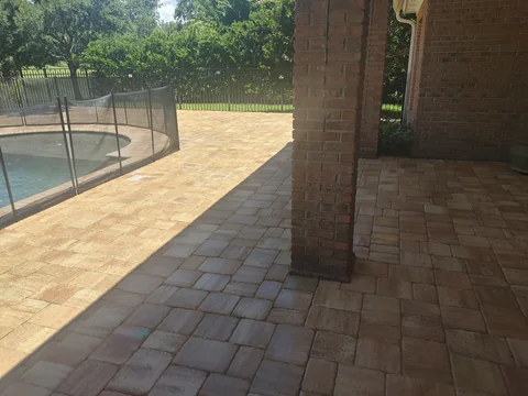 Tan paver pool deck and covered patio beside a brick home