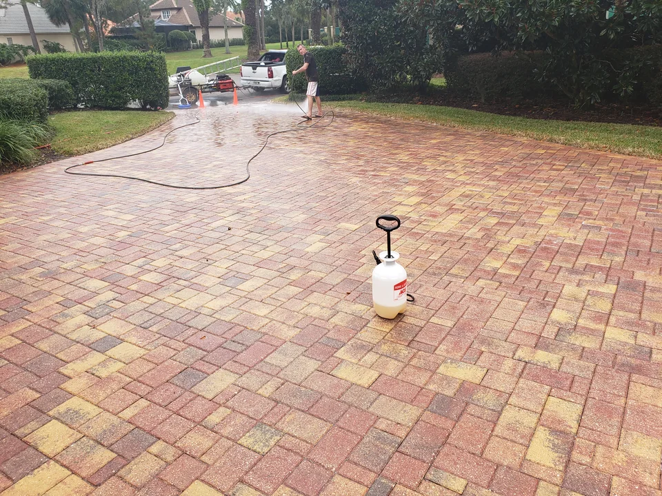 Safe Touch cleaning a red and gold brick paver driveway with a technician and wash equipment on site