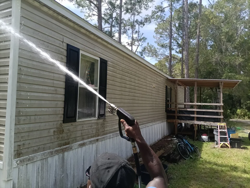 Safe Touch applying a house-washing solution to vinyl siding with visible exterior buildup