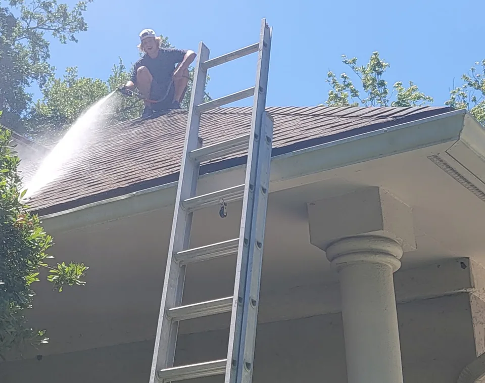 Safe Touch technician rinsing a shingle roof beside an access ladder