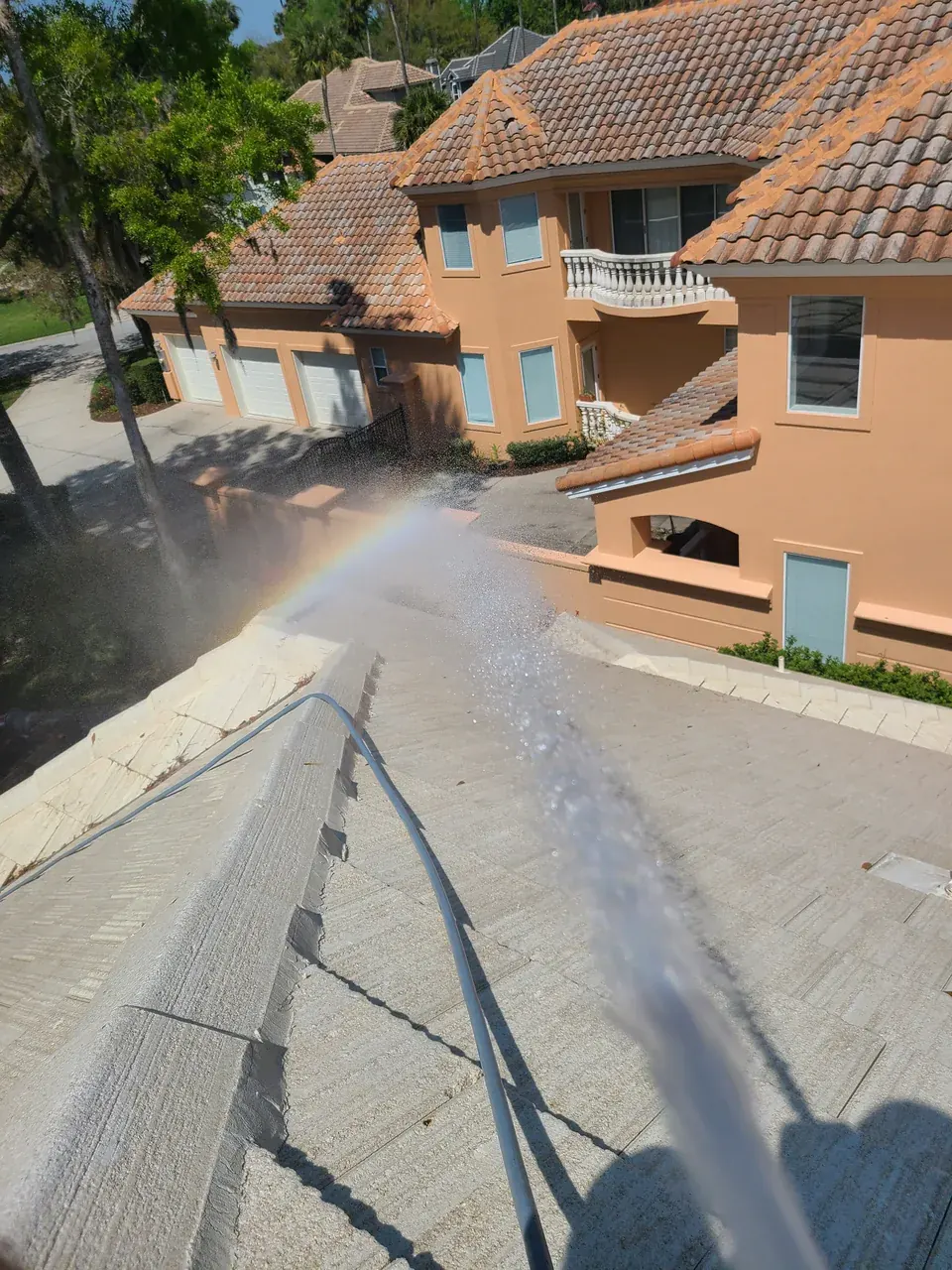 Water rinsing a light-colored tile roof with a tiled neighboring home in the background